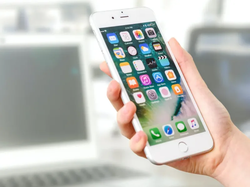 Une main tient un téléphone dont l'écran affiche une grille d'applications