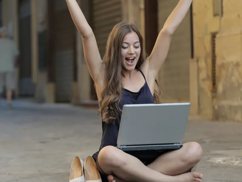 Une femme lève les bras devant son ordinateur portable, assise dehors