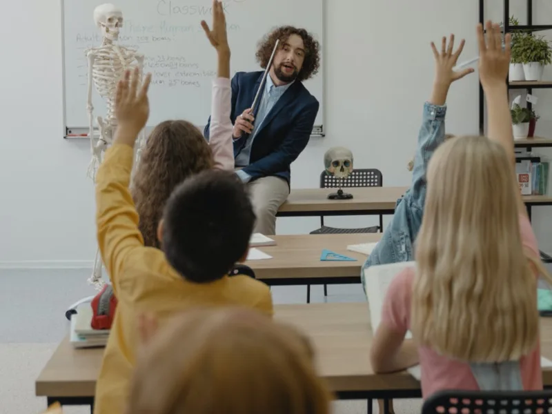 Une classe lève la main devant un enseignant, au tableau